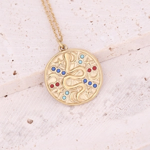 Macro view of a gold pendant with an engraved snake, moon, stars, and colorful gemstones