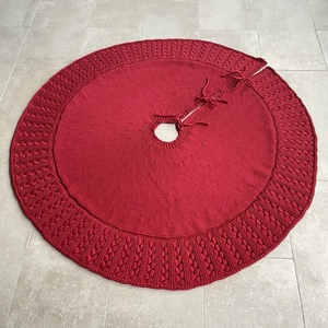 Detail of dark red knitted Christmas tree skirt with cable stitch patterns and ties