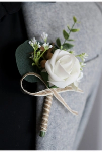 Close-up of a white silk rose boutonniere with burlap ribbon on a grey suit jacket