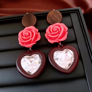 Macro detail of vintage wooden heart earrings with pink rose and sparkling rhinestones