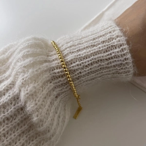 Close-up of minimalist 925 sterling silver gold beaded bracelet on a knit sleeve