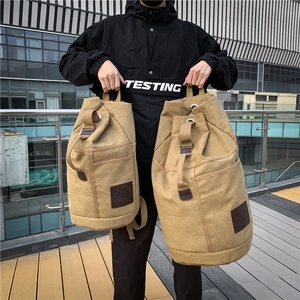 Outdoor canvas cylinder travel backpack in khaki showing two sizes held by a model