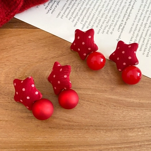 Detailed close-up of red polka dot fabric star earrings with large red pearls on wood