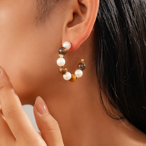 Detail of C-shaped 16K gold earrings with pearls and tiger eye beads on a model