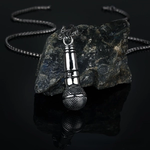 Detailed close-up of a silver microphone pendant on a rugged dark stone background