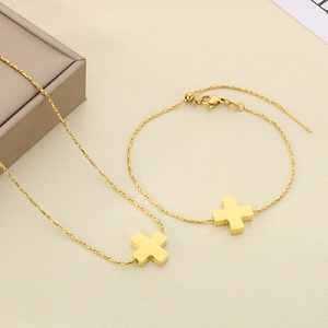 Detail of gold cross pendant necklace and adjustable bracelet set on beige fabric