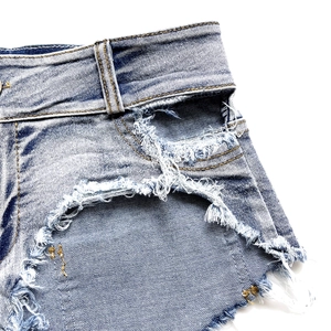 Dettaglio macro dei pantaloncini in denim blu scuro con bordi strappati e trama invecchiata