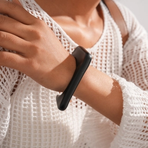 Close-up of a matte black geometric open cuff bracelet worn with a white knit sleeve