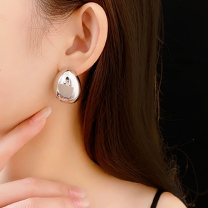 Gros plan d'une boucle d'oreille goutte d'argent portée à l'oreille sur fond noir
