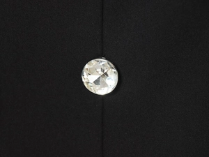 Detail of a round white rhinestone button on textured black fabric shorts