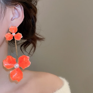 Detail of long orange flower earrings with white pearl centers worn by model