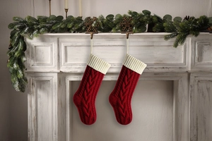 Close-up of red cable knit Christmas stockings hanging from snowflake hooks on a fireplace