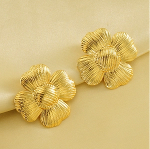 Detail of gold floral stud earrings with textured finish on soft beige silk background