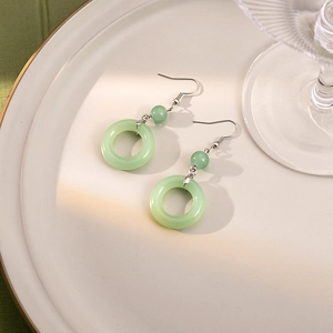 Macro shot of green faux jade beaded earrings with silver hooks on a decorative plate