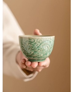 Close-up of celadon ceramic teacup with embossed dragon motif held in hands