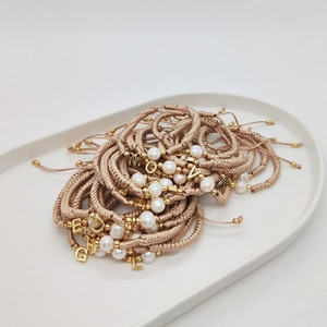 Handmade woven pearl bracelet with gold initial charms in a white ceramic tray