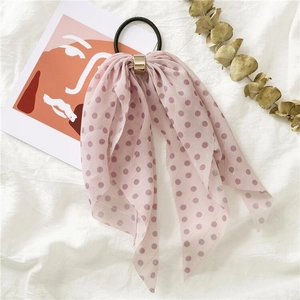 Pink polka dot hair scrunchie with long ribbons and a gold buckle on white fabric