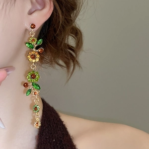 Nahaufnahme der goldenen Blumenohrringe mit smaragdgrünen und bernsteinfarbenen Kristallen
