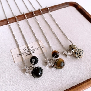 Detailed view of three tiger eye pony pendants with beaded chains on a white tray