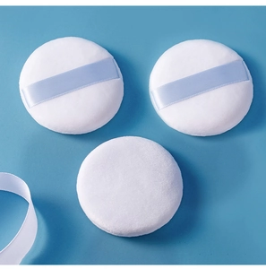 Detailed view of three soft round powder puffs in white with light blue ribbon handles