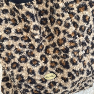 Detailed macro view of leopard print faux shearling fabric with a gold logo metal plate