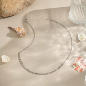 Detailed view of silver stainless steel necklace with curved bar pendant on beach backdrop