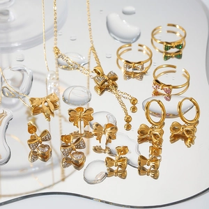 Artistic layout of gold bow jewelry set with crystal accents on reflective water mirror