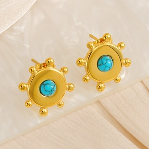 Gros plan de boucles d'oreilles en acier doré et turquoise sur un tissu en soie blanc