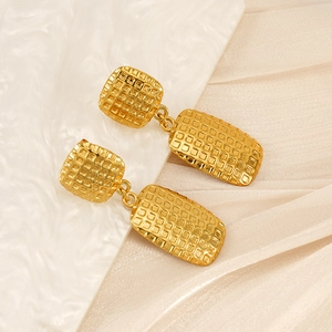 Close-up of golden geometric earrings with textured grid pattern on soft fabric
