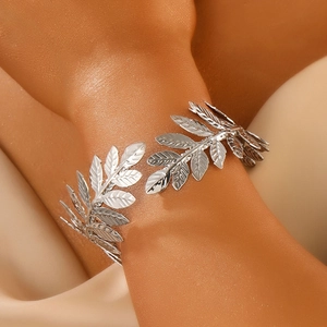 Close-up of a silver olive leaf open bangle worn on the arm against a satin background