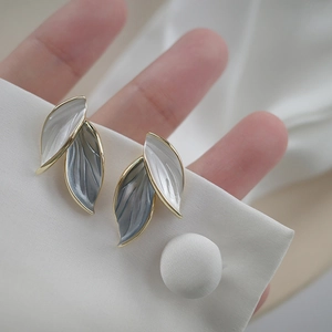 Macro detail of elegant double-layered leaf earrings with gold edges on white fabric