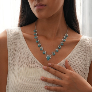 Detail view of a V-shaped necklace with turquoise teardrop stones on a white knit sweater