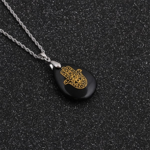 Detailed close-up of Hamsa hand pattern on a black teardrop pendant with silver chain