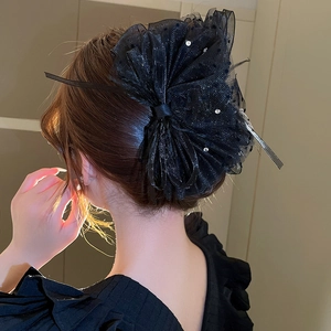 Gros plan d'une pince à cheveux nœud en mesh noir avec strass portée par le modèle