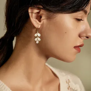 Close-up of cat eye stone leaf earrings with diamonds worn by a model in soft light
