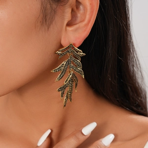 Détail macro de boucles d'oreilles feuilles dorées avec strass noirs sur modèle