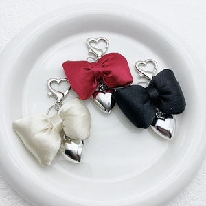 Three satin bow keychains in wine red black and cream with silver heart pendants on tray