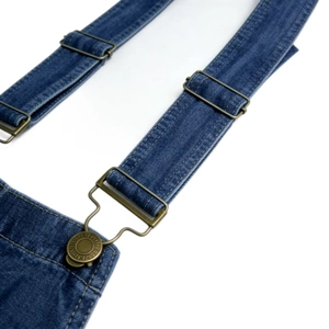 Close-up of adjustable bronze metal buckle and denim shoulder strap on blue overalls