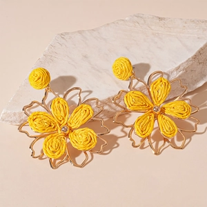 Pendientes de flores de rafia amarilla con tachuelas doradas sobre base de piedra