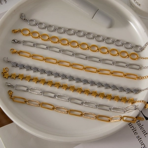 Detail of 18K gold and silver stainless steel paperclip chain bracelets on white ceramic tray