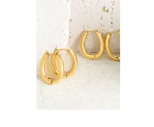 Close-up of polished gold U-shape earrings on a textured stone surface with a soft glow