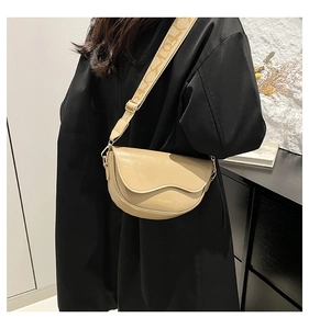 Model wearing a beige crescent saddle bag with a wide logo-patterned shoulder strap