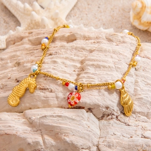 Detail of 18k gold plated seahorse and shell charms with colorful beads on a sandy beach