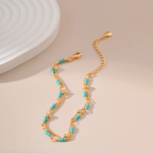 Detail of double-layer gold chain bracelet with turquoise beads and heart pendant