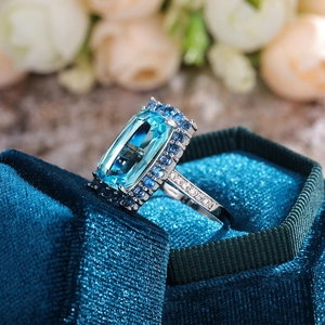 Détail macro d'une bague avec zircon bleu rectangulaire et halo dans un écrin en velours