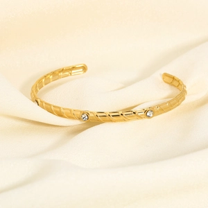 Detailed view of golden cuff bracelet with twisted texture and inlaid zircons