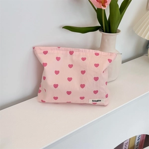Detail of pink canvas tote bag with heart patterns and zipper closure on a white table