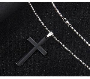 Detailed close-up of a black cross pendant on a silver box chain over dark texture