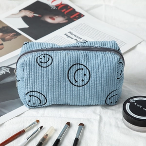 Detail of light blue corduroy makeup bag with smiley pattern on a fashion magazine background