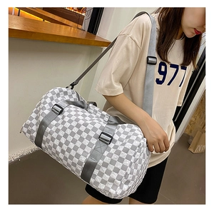 Detail view of a grey checkerboard travel bag carried by a model on a shoulder strap